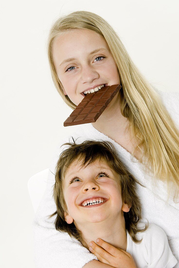 Mädchen beisst in Schokoladentafel, kleiner Junge davor