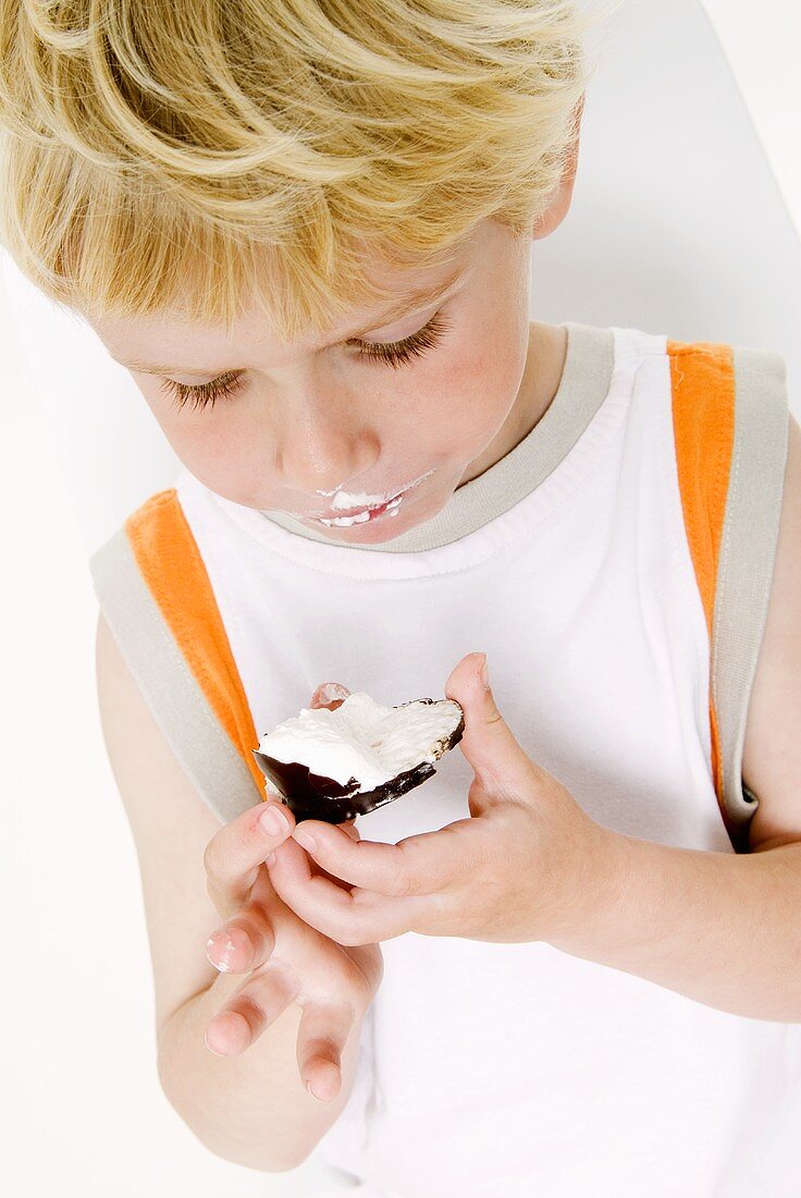 Small boy eating a chocolate-covered marshmallow wafer