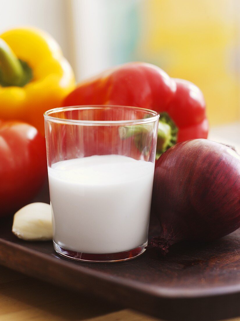 A glass of coconut milk with vegetables in background
