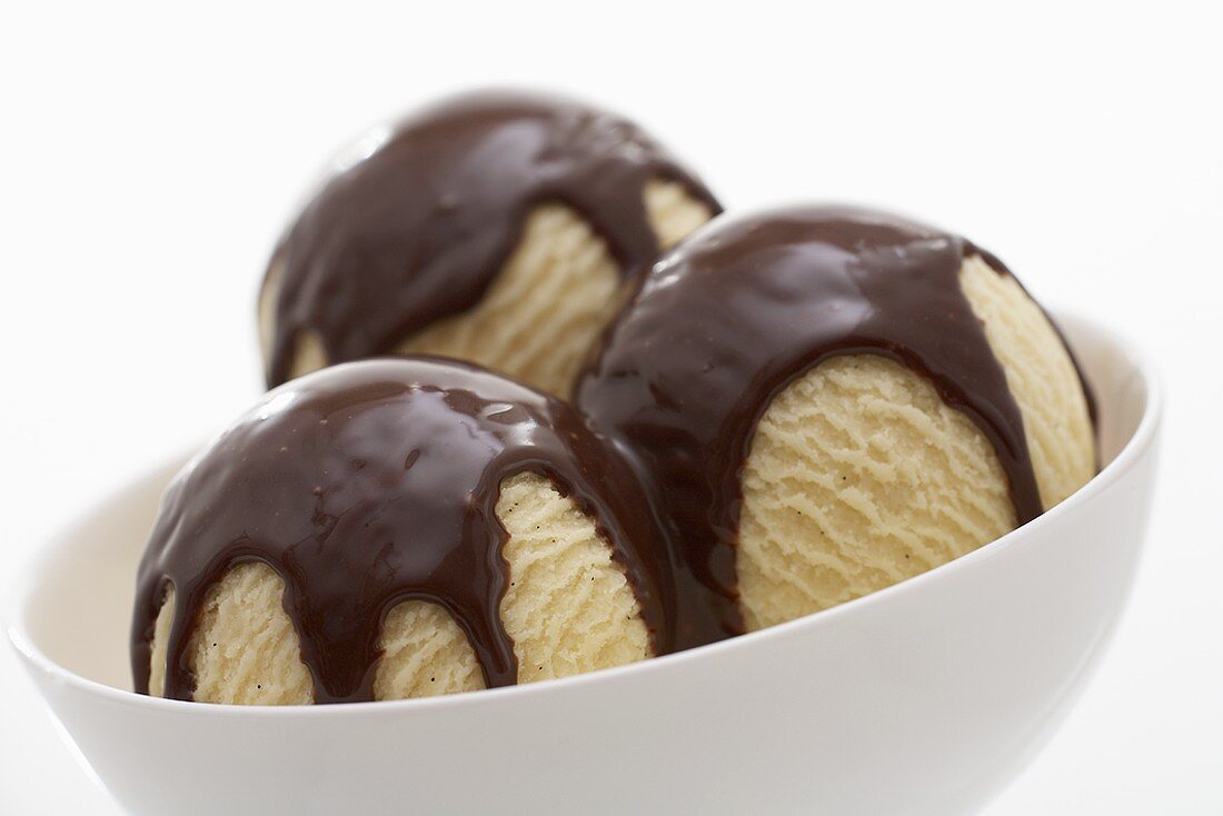 Three scoops of vanilla ice cream with chocolate sauce in dish