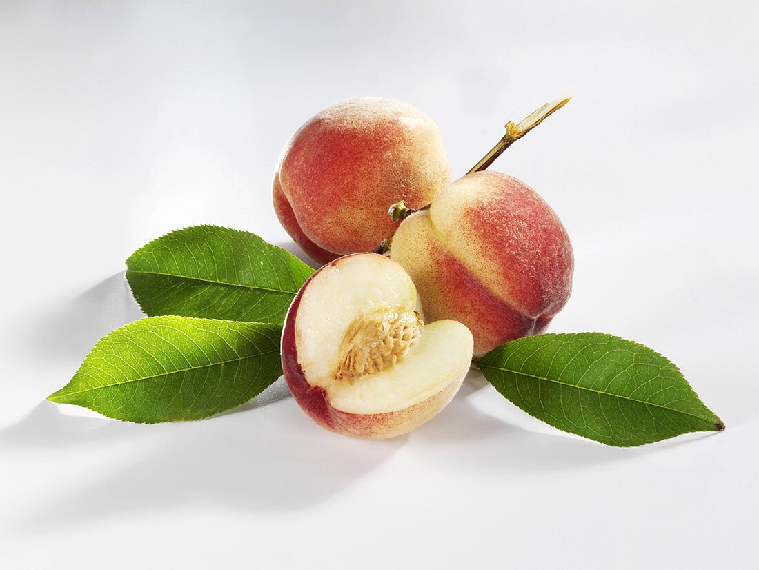 Two whole peaches and part of a peach with twig and leaves