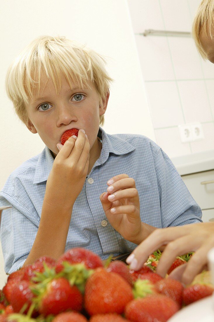 Blonder Junge beisst in eine Erdbeere