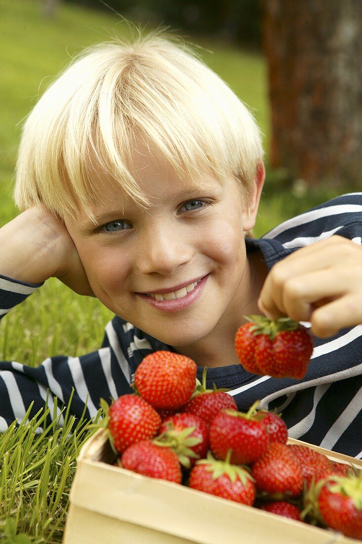 Blond boy lying in grass with a basket of strawberries