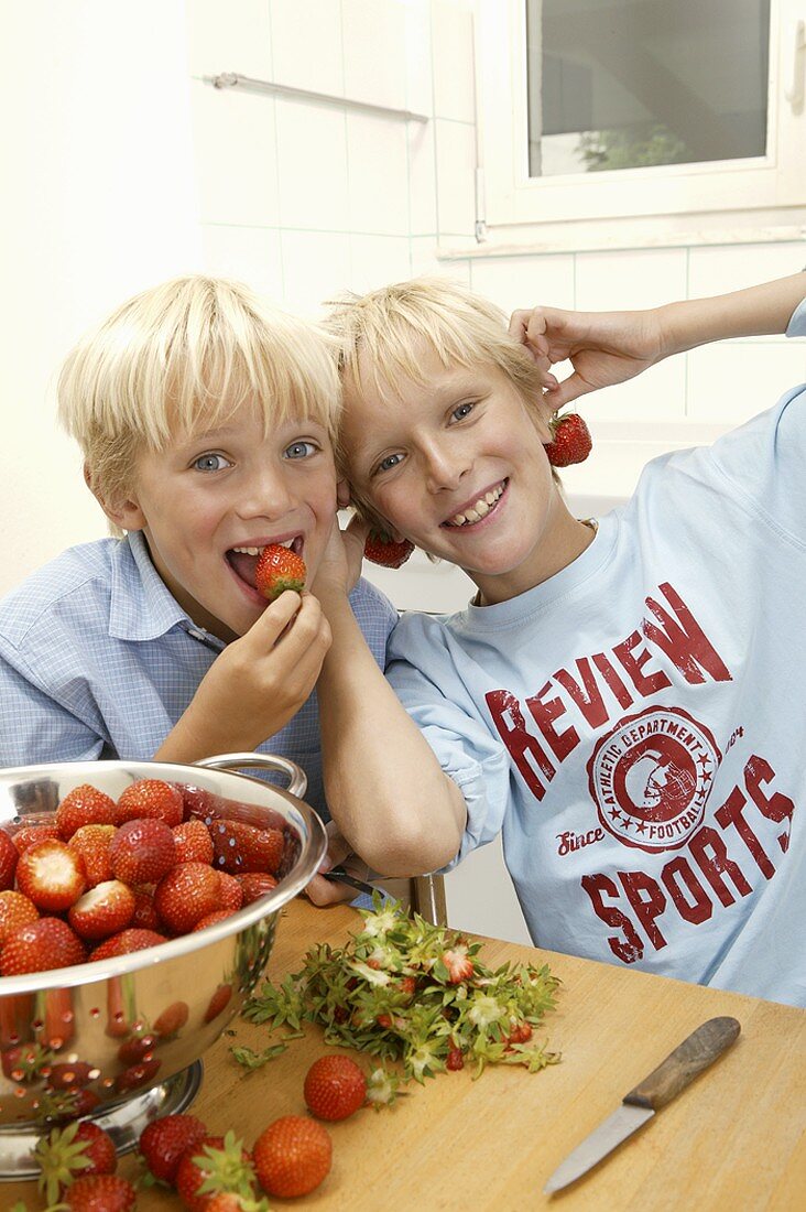 Two blond boys hulling strawberries