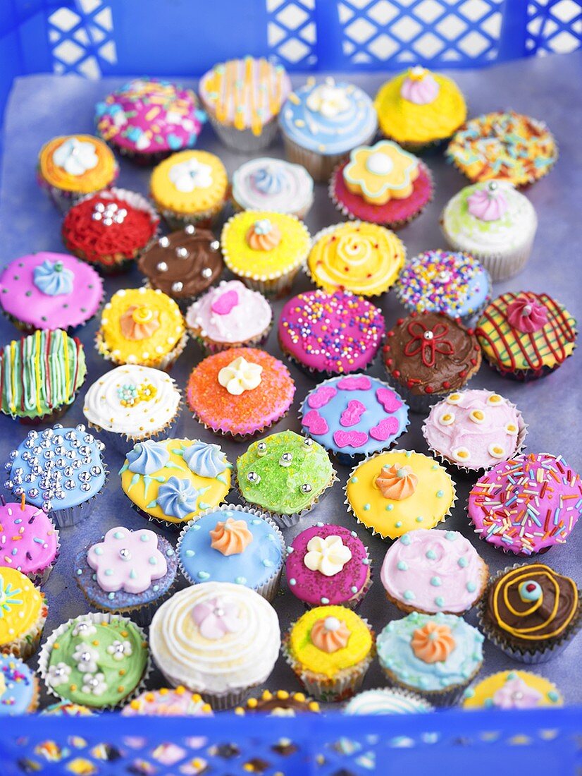 Cupcakes with colourful decorations in a baker's tray