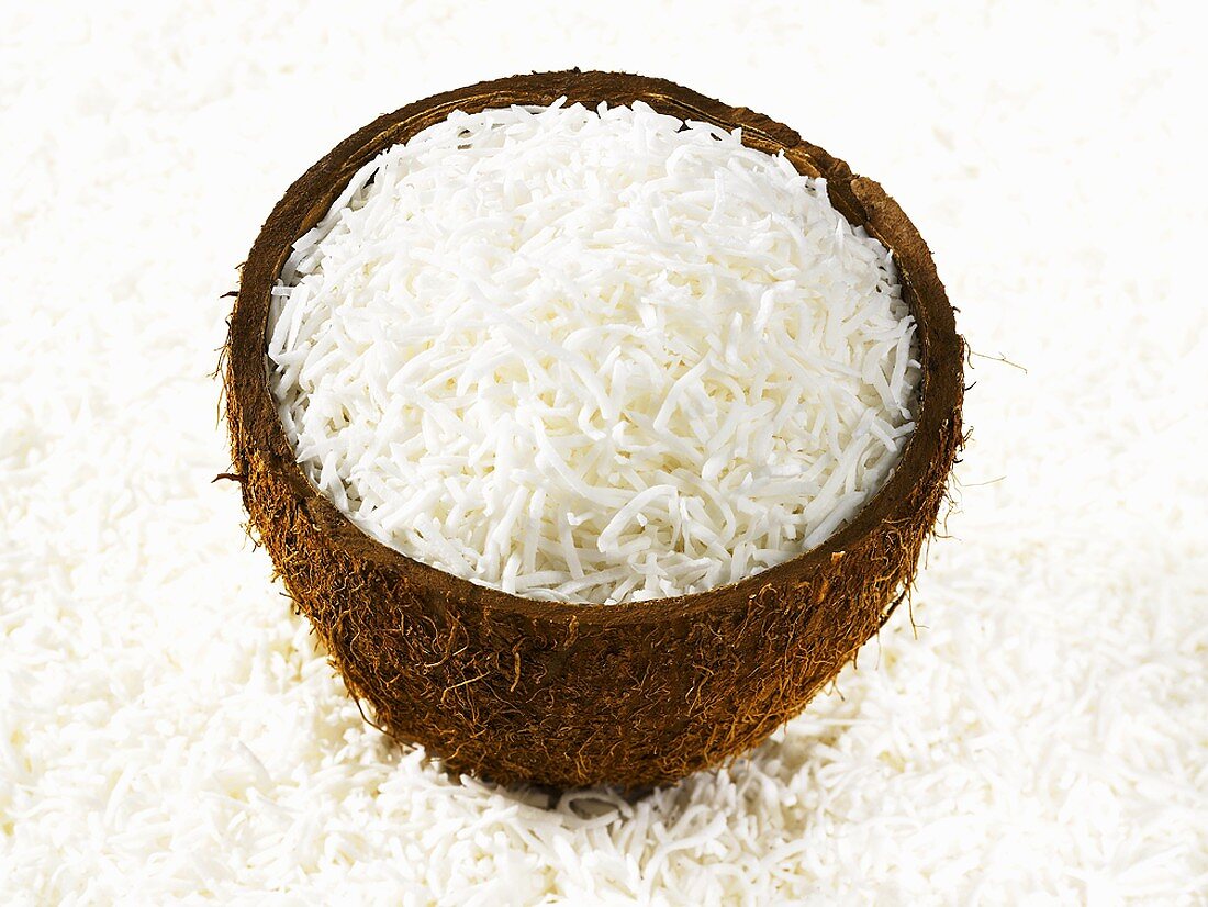 Grated coconut in half coconut shell surrounded by grated coconut