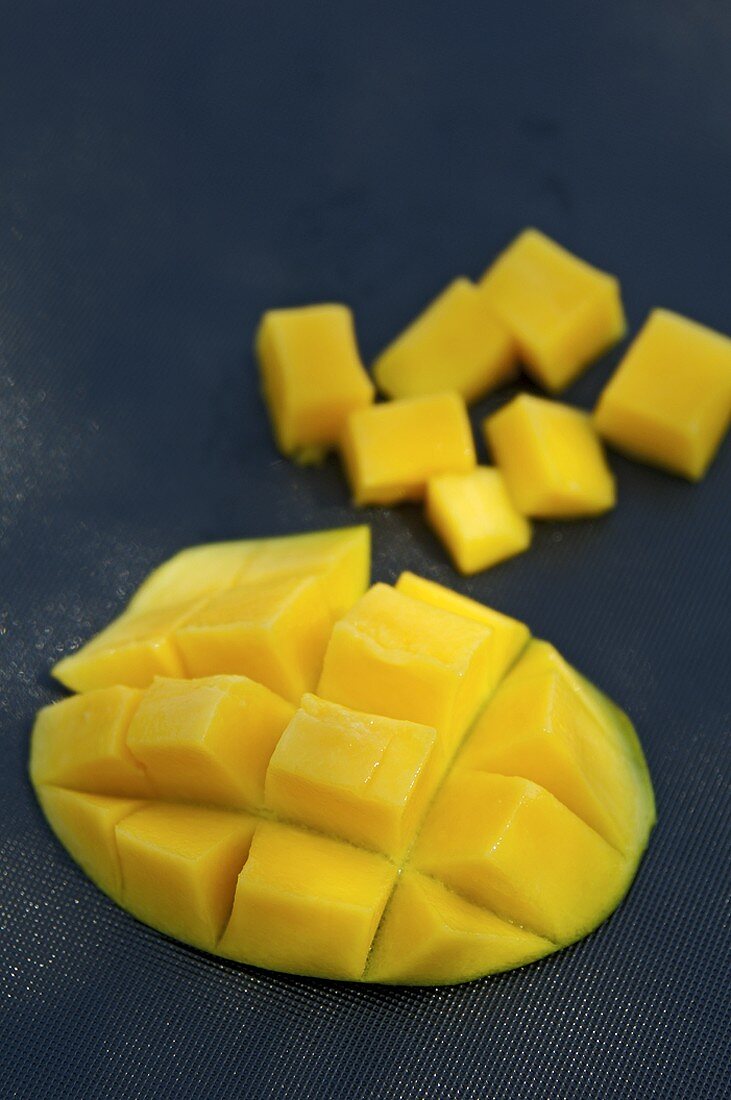 A mango half cut into cubes and cubes of mango
