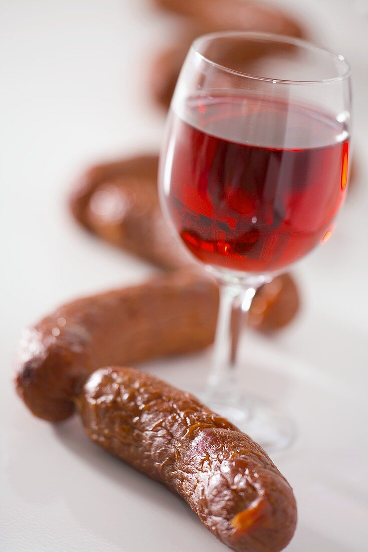 A glass of red wine surrounded by sausages