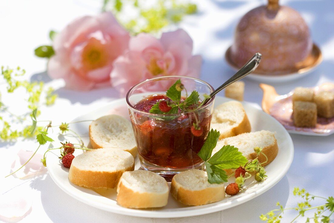 Wild strawberry jam in glass with baguette slices