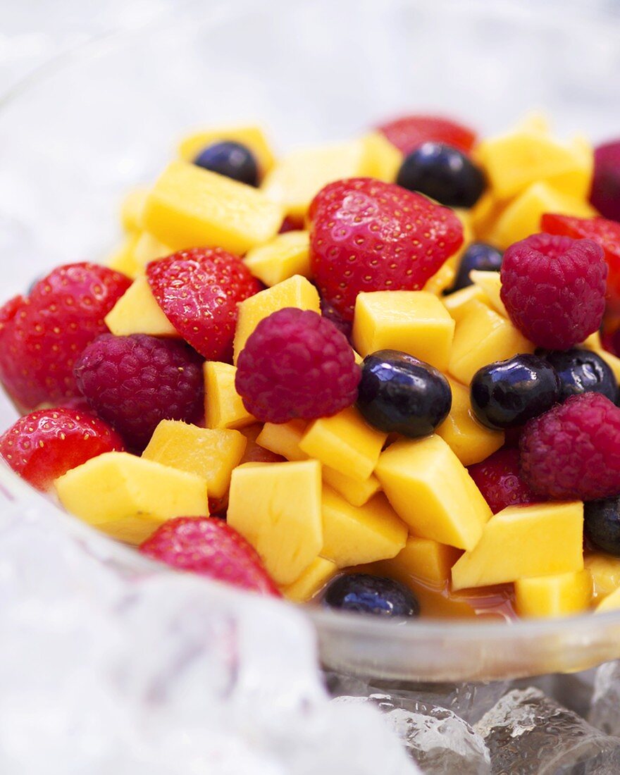 A bowl of mango and mixed berry salad with vodka on ice