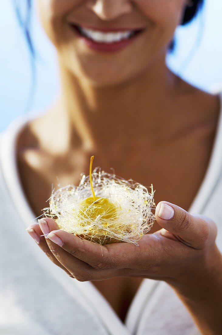 A woman holding a a mirabelle in a nest of angel's hair