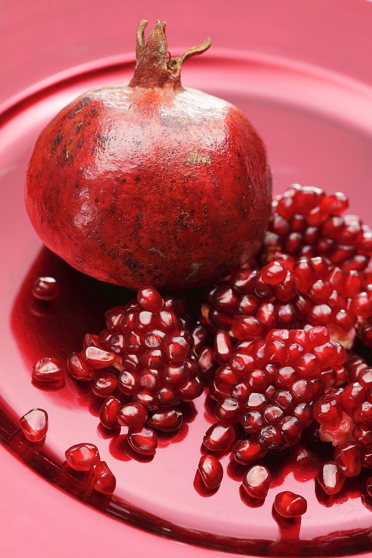 A pomegranate and pomegranate seeds on a red plate