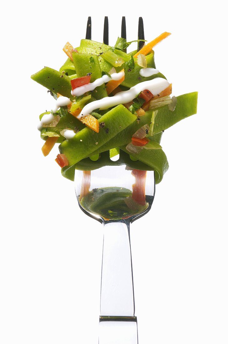 Green ribbon pasta with vegetables and sauce on a fork