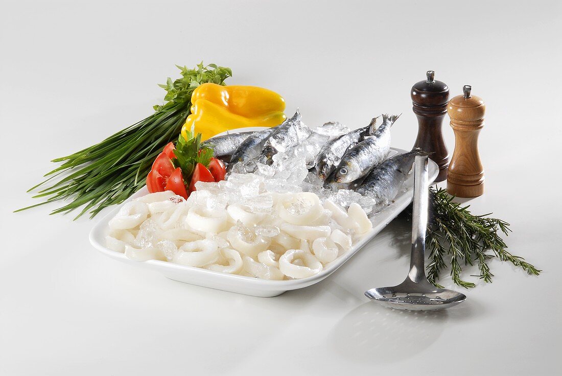 Tintenfischringe und Sardinen auf Eis mit Kräutern und Gemüse