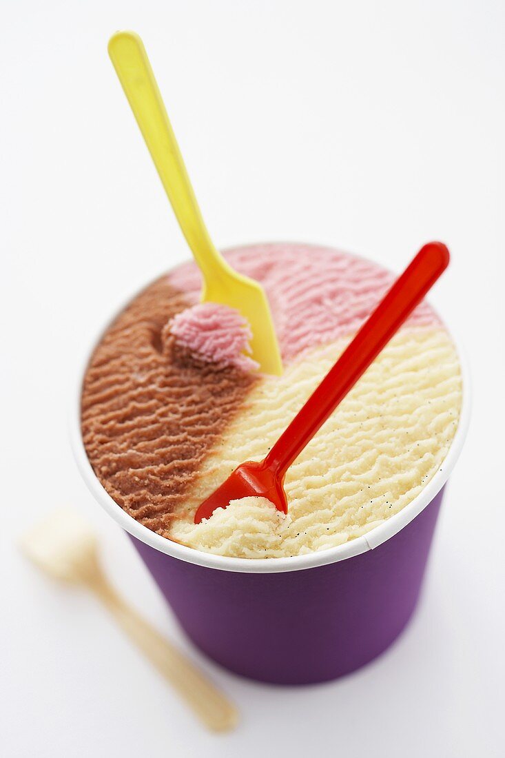 Neapolitan ice cream in tub with plastic spoons