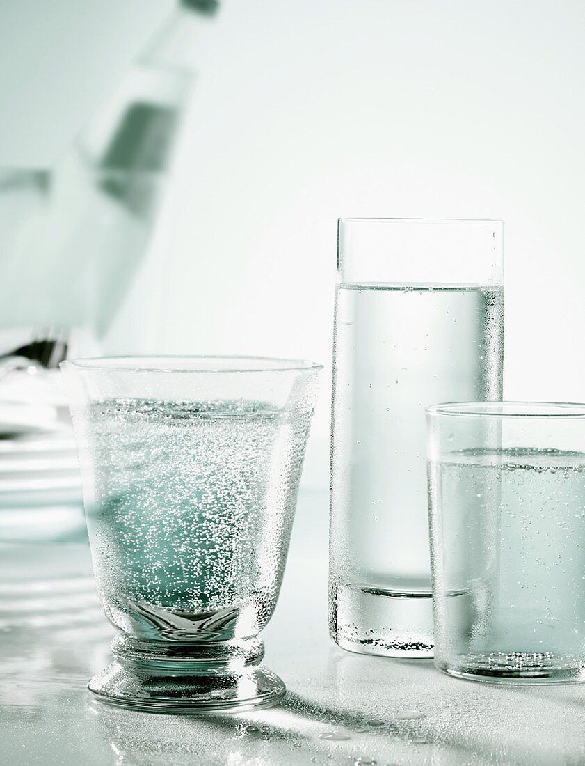 Three glasses of mineral water with bottle in background