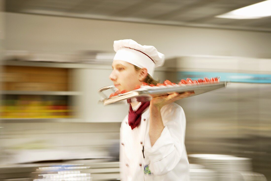Junger Koch trägt Tablett mit Erdbeertörtchen