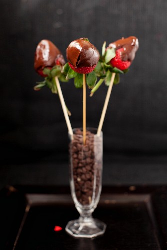 Drei Schokoladenerdbeeren auf Spiessen in einem Glas mit Chocolatechips