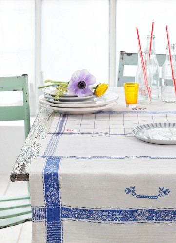 Blue and white tea towels used as tablecloth, anemones on stacked plates and bottles on rustic kitchen table