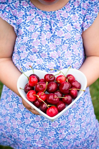 A girl holding a heart-shaped dish of cherries