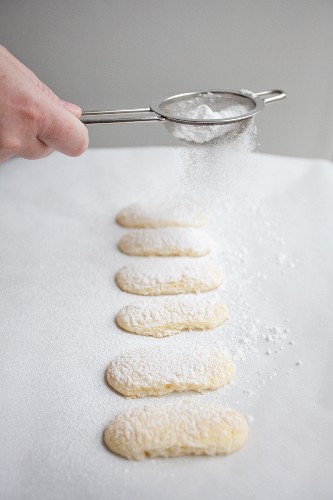 Sponge fingers being dusted with icing sugar