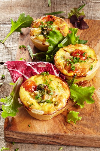 Three mini vegetable quiches with a salad garnish on a wooden board