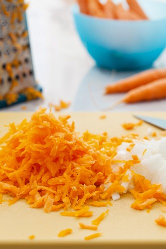 Grated carrots and diced onions on a cutting board