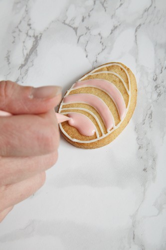 An egg-shaped biscuit being decorated with icing