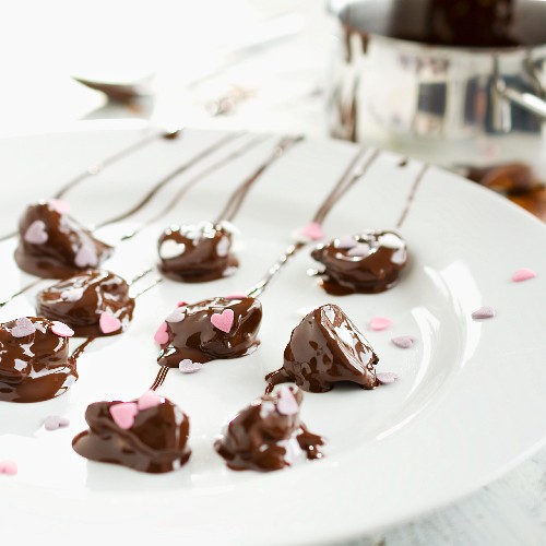 Chocolate-covered plums decorated with sugar hearts being made