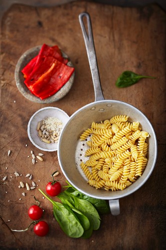 Cooked fusilli in a colander with ingredients for pepper sauce
