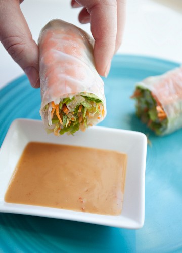 A woman dipping of rice paper roll into a dish of peanut sauce