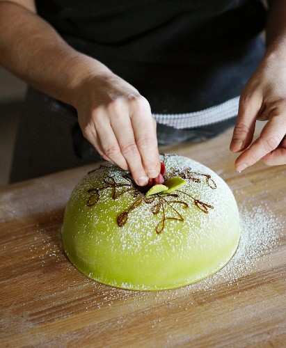 A Princess cake being decorated with a marzipan rose