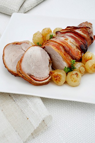 Pork fillet wrapped in bacon with white onions
