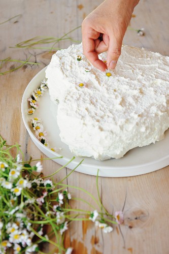 A heart-shaped creamy carrot cake being decorated with daisies