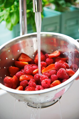 Raspberries and strawberries being washed in a colander