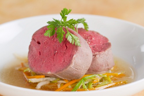 Poached fillet steak on a bed of vegetables with broth