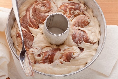 Light and dark marble cake batter in a cake mould, mixed with a fork