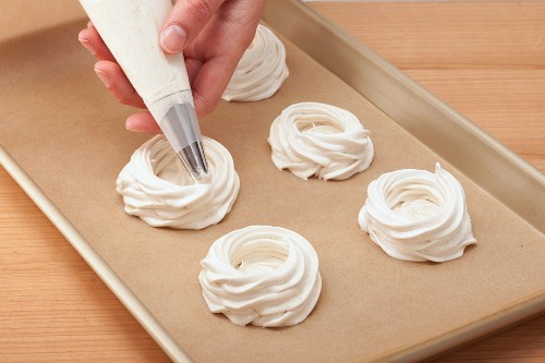 A hand piping meringue nests onto a baking tray