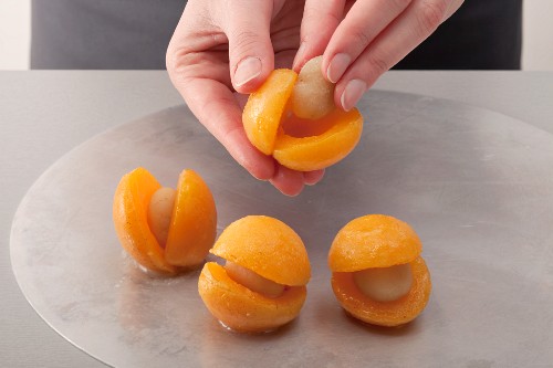 Hand füllt Aprikosen mit Marzipan