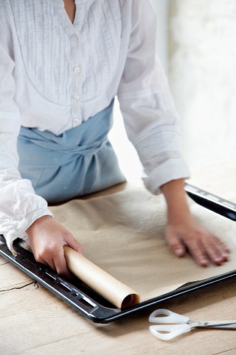 A baking tray being lined with baking paper