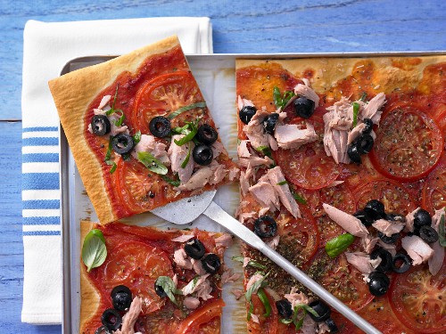 A tomato and tuna pizza with black olives and basil