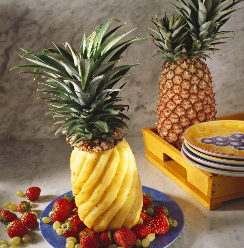 A whole fresh pineapple cut in a swirl pattern with berries