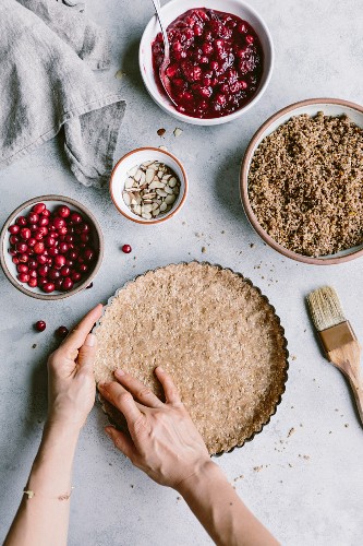 A woman is prepping the dough for a cranberry almond tart