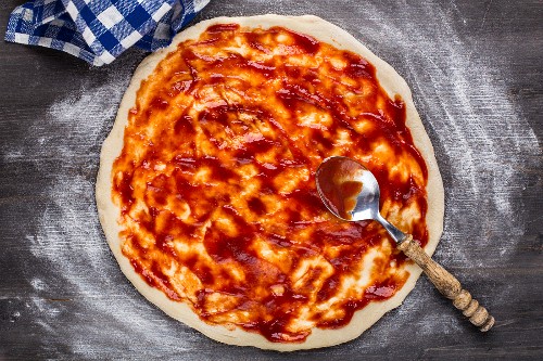 Pizza zubereiten: Pizza mit Tomatensauce bestreichen (Aufsicht)