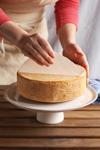 Female hands peeling the parchment paper from the bottom of the sponge cake