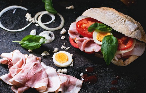 Sandwich with ham, eggs, vegetables and ketchup, served with french fries over black background