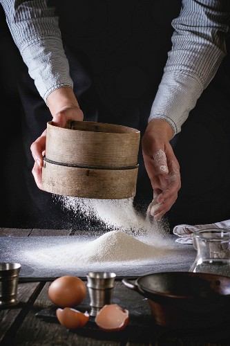 Female hands sifting flour from old sieve on old wooden kitchen table