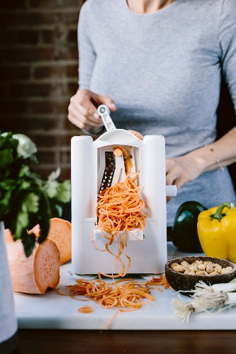 A woman is spiralizing sweet potato to turn them into noodles