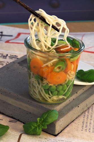 Asian noodle soup with peas, carrots and basil in a glass