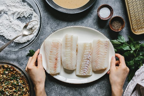 A woman is placing four cod fillets on the table